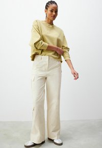 Sudadera verde deschis scurtă cu textul "MALIBU CALIFORNIA", combinată cu pantaloni bej cu picioare largi, care au buzunare laterale și un finisaj neted.