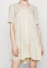 Abito a maniche corte, con scollo a V, di un pallido beige con pois neri, orlo arricciato e dettagli con bottoni, realizzato in tessuto leggero.