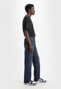 Zwarte T-shirt met korte mouwen gecombineerd met donkerblauwe straight-leg jeans en zwart-witte sneakers. Zichtbare zijzakken en rechte naden.