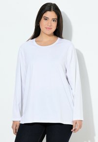 Witte langekorte mouw t-shirt met een ronde halslijn en een lose fit, gemaakt van zacht materiaal, weergegeven naast donkere spijkerbroek.