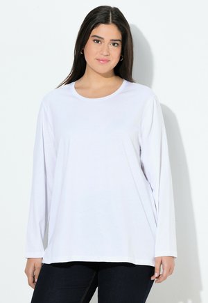 Camiseta blanca de manga larga con cuello redondo y corte relajado, hecha de material suave, expuesta junto a unos pantalones vaqueros oscuros.