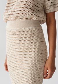 Beige gestricktes Oberteil und Rock mit einem offenen, strukturierten Muster. Besitzt einen gerippten Taillenbund und zeigt ein figurbetontes Design sowie atmungsaktiven Stoff.