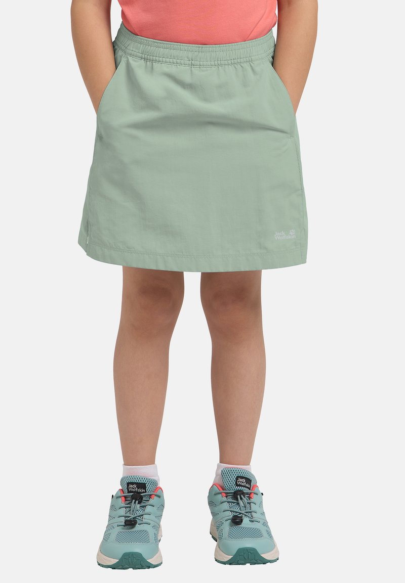 Enfant portant une jupe vert menthe avec une taille élastique et des chaussures de randonnée vert menthe avec des lacets noirs et le logo Jack Wolfskin.