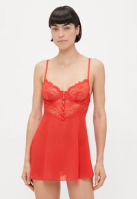 Nuisette en dentelle rouge et en tissu transparent, dotée de bretelles spaghetti réglables et d'un détail de fermeture à boutons sur le devant. Longueur mi-cuisse avec une coupe ample.
