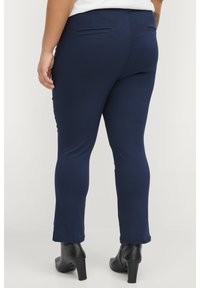 Navy blue fitted pants with a smooth texture, featuring a back pocket, and finished with a tailored hem, paired with black heeled ankle boots.