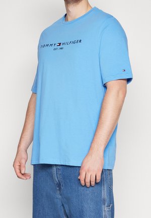 Light blue cotton T-shirt with short sleeves and a crew neckline, featuring a dark logo text across the front and a small accent at the sleeve.