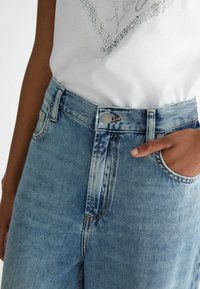Light blue denim jeans with a high waist, featuring a button closure, front pockets, and subtle fading along the fabric surface.