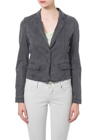 Szary skórzany blazer w miękkim materiale, z klapami, dwoma guzikami i przednimi kieszeniami. Zestawiony z jasnymi spodniami.