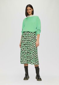 Sweatshirt vert menthe avec texte en relief, associé à une longue jupe à motif géométrique noir, vert et beige. Bottines noires.