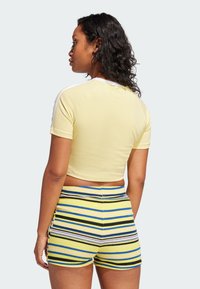 Yellow cropped t-shirt with white shoulder stripes, paired with striped shorts featuring blue, black, and purple lines on a yellow background.