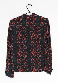 Chemise à manches longues avec un fond sombre présentant un motif abstrait de serpent en rouge vif et bleu sarcelle. Tissu doux avec une coupe décontractée.