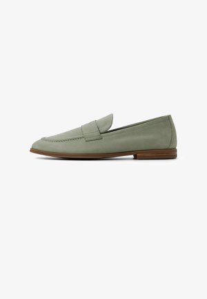Mocassino verde in suede con suola marrone e tacco basso impilato, caratterizzato da una fascia cucita sulla parte superiore.
