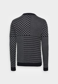 Pull tricoté avec des motifs géométriques en noir et blanc, comprenant des rayures, des chevrons et des losanges, avec un col rond et des manches longues.