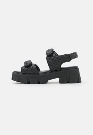 Sandalias de plataforma negras acolchadas con suelas gruesas y estriadas, que cuentan con dos correas ajustables y un diseño de espalda abierta.
