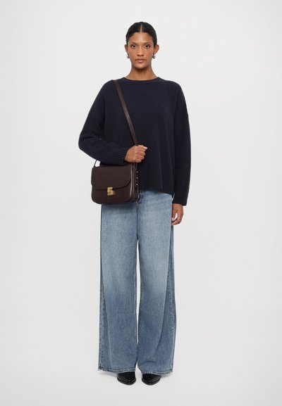 Maglione lavorato navy, jeans larghi di jeans azzurri, scarpe nere e una borsa a tracolla in pelle marrone con accessori in oro.