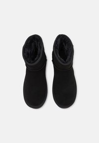 Stivaletti neri in suede con una morbida fodera in pelliccia. Presentano una punta arrotondata e un'apertura a risvolto, con dettagli cuciti sui lati.