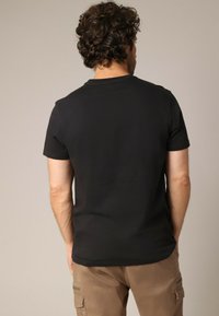 Chemise noire à manches courtes en coton, avec un col rond et une texture lisse, portée avec un pantalon cargo beige.