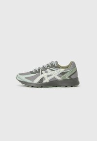 Sport shoe featuring a grey mesh upper with green accents, light reflective details, flat laces, and a textured sole for grip.