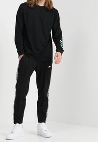 Svart långärmad t-shirt med färggrafik på ärmen, kombinerad med svarta smala joggers med en vit rand och Nike-logotyp.