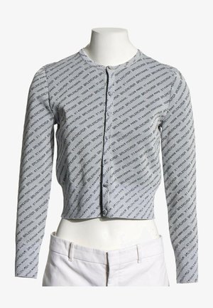 Cardigan gris à manches longues cropped avec motif de texte noir en diagonale et boutons sur le devant, présenté sur un buste de mannequin blanc.