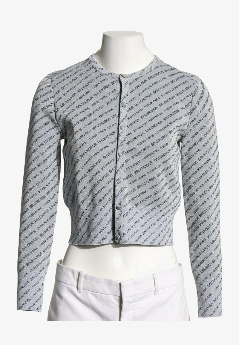 Cardigan gris à manches longues cropped avec motif de texte noir en diagonale et boutons sur le devant, présenté sur un buste de mannequin blanc.