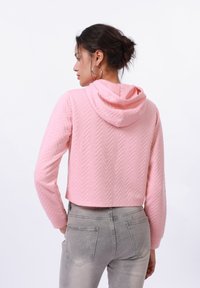 Felpa corta rosa chiaro con un motivo a spina di pesce testurizzato e cappuccio con cordino, abbinata a jeans grigi aderenti.