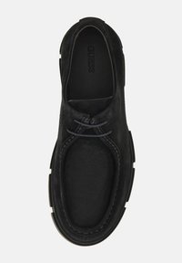 Fekete velúr, slip-on cipő minimális fűzéssel, kerek orral és textúrált talppal. Finom varrási részletek találhatók a szélek mentén.
