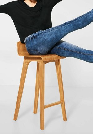 Puuistuime, millel on sile looduslik viimistlus; inimene istub denim teksade ja musta särgiga, jalad välja sirutatud, juhuslik poos.