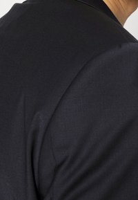Blazer nero su misura, con tessuto morbido, spalle strutturate e dettagli di cucitura precisi, che enfatizzano un design elegante.