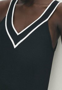 Canottiera nera con scollatura a V profonda e bordi bianchi, caratterizzata da una texture a coste. Spalline sottili e design aderente enfatizzano la struttura.