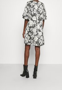 Kwiatowa sukienka w czarno-białym wzorze, z krótkimi bufiastymi rękawami i prostą sylwetką. Dopasowana do błyszczących, czarnych botków za kostkę.