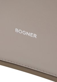 Matériau synthétique gris clair avec une texture lisse, arborant le logo blanc "BOGNER" et de subtils détails de couture sur le bord.
