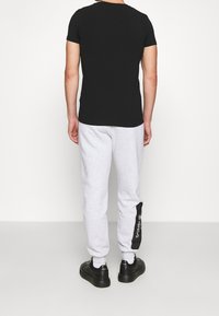 Svart kortärmad t-shirt och grå träningsbyxor med en sidologo, i kombination med svarta sneakers. Outfiten framhäver en avslappnad stil.