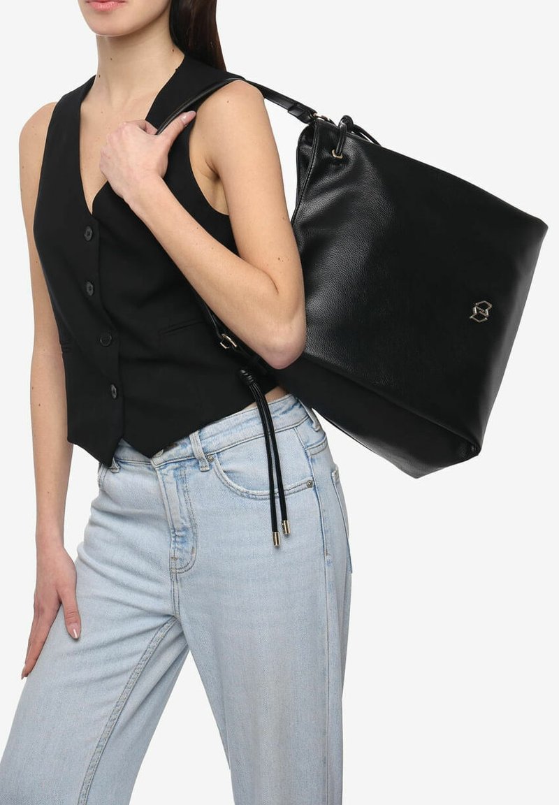 Borsa a secchiello in pelle nera con texture liscia, hardware in tonalità oro, chiusura con coulisse e un accentuazione del logo. Indossata a spalla.