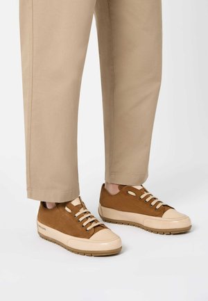 Braune Wildleder-Sneaker mit beigen Gummisohlen und Zehenkappen, ausgestattet mit beigen Schnürsenkeln und dezenten Perforationen, kombiniert mit hellbeigen Hosen.