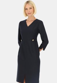 Granatowa sukienka o długości do kolan, z dekoltem w kształcie litery V, rękawami o długości trzy czwarte i złotymi guzikami na wysokości talii. Gładka faktura i dopasowany krój.