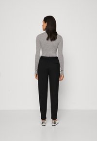 Gray long-sleeve top paired with black tapered pants, featuring a slim fit. Silver shoes complete the outfit, shown from the back.
