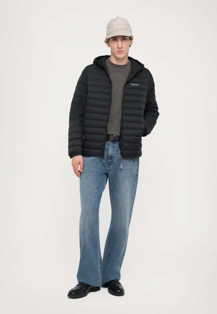 Doudoune noire avec capuche, pull gris texturé, jeans évasés bleu clair, et chaussures noires, complétés par une casquette gris clair.