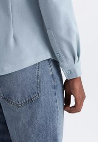 Lichtblauw langemouw shirt van textuurstof, met knoopmanchetten en een gebogen zoom, gecombineerd met lichtblauwe denim jeans.