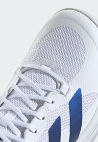 Biały but sportowy z oddychającą cholewką z siateczki, teksturowanymi detalami, płaskimi sznurowadłami i niebieskimi syntetycznymi nakładkami. Płaska, gładka gumowa podeszwa.