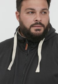 Felpa con cappuccio nera con zip realizzata in tessuto morbido, dotata di lacci crema, chiusura con zip e un'etichetta con logo sul colletto.