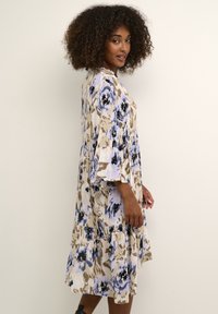 Robe florale avec manches cloche, design mi-genou, dans des nuances de bleu, crème et marron, avec un ourlet à volants en couches et une texture de tissu douce.