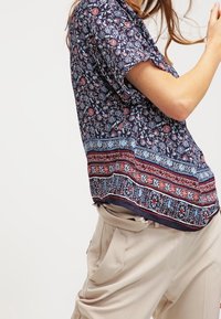 Tummansininen kukkakuosiset pusero lyhyillä hihoilla, jossa on kontrastivärinen kuviollinen alahelma punaisen ja sinisen sävyissä. Pehmeä kangas.