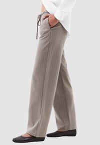 Pantaloni a gamba larga grigio chiaro con righe bianche, vita elastica, cordoncino regolabile e tasche laterali. Abbinati a scarpe basse nere.