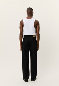 Λευκή φανέλα χωρίς μανίκια και μαύρο παντελόνι με φαρδύ πόδι. Το παντελόνι διαθέτει διακριτικό σχέδιο και πίσω τσέπη με ταμπέλα σε καφέ χρώμα. Ύφασμα απαλό και άνετη εφαρμογή.