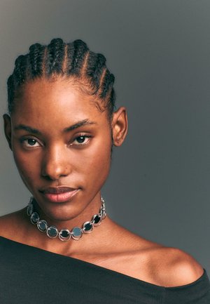 Czarny naszyjnik choker z naprzemiennymi srebrnymi okrągłymi i czarnymi okrągłymi ogniwami, noszony z czarną bluzką bez ramion na szarym tle.