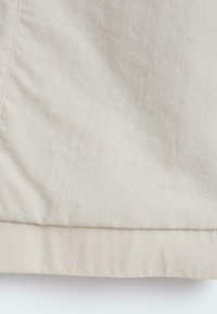 Gros plan sur un tissu beige avec des coutures et un bord ourlé sur un vêtement.