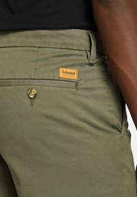 Timberland khaki bukser i slidstærkt stof har en knaplukning, baglomme og et mærket lædertag på linningen.