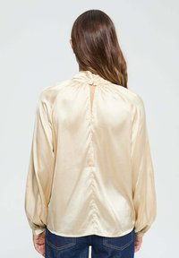 Blouse en satin à manches longues de couleur beige pâle, dotée d'un col montant avec tissu froncé, d'une ouverture en forme de goutte dans le dos et de poignets élastiques.