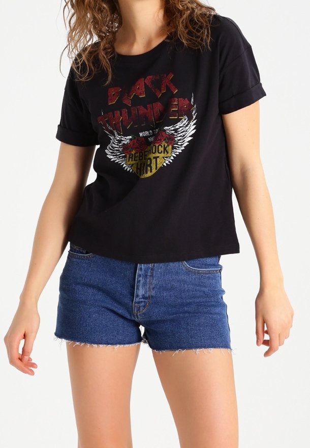 Camiseta gráfica negra con mangas enrolladas que presenta un diseño de texto rojo y alas blancas, combinada con pantalones cortos de mezclilla azul con bordes deshilachados.